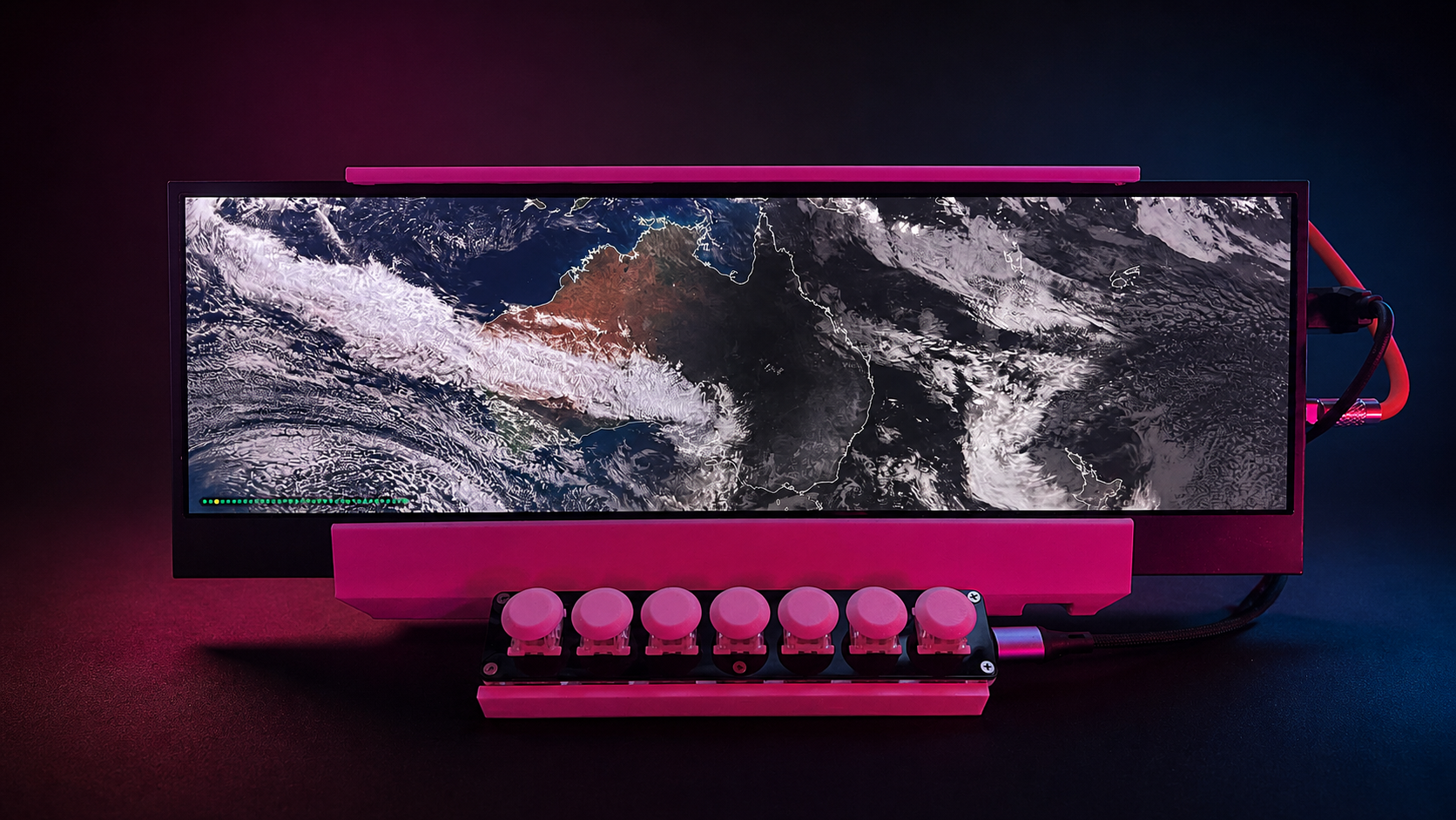Ultrawide home kiosk displaying a satellite view of Australia, mounted in a pink 3D-printed frame with a seven-button switcher below